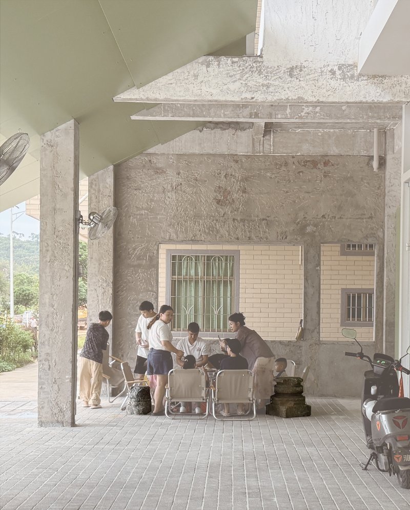 Covered outdoor porch with concrete columns where visitors gather around folding chairs in afternoon light