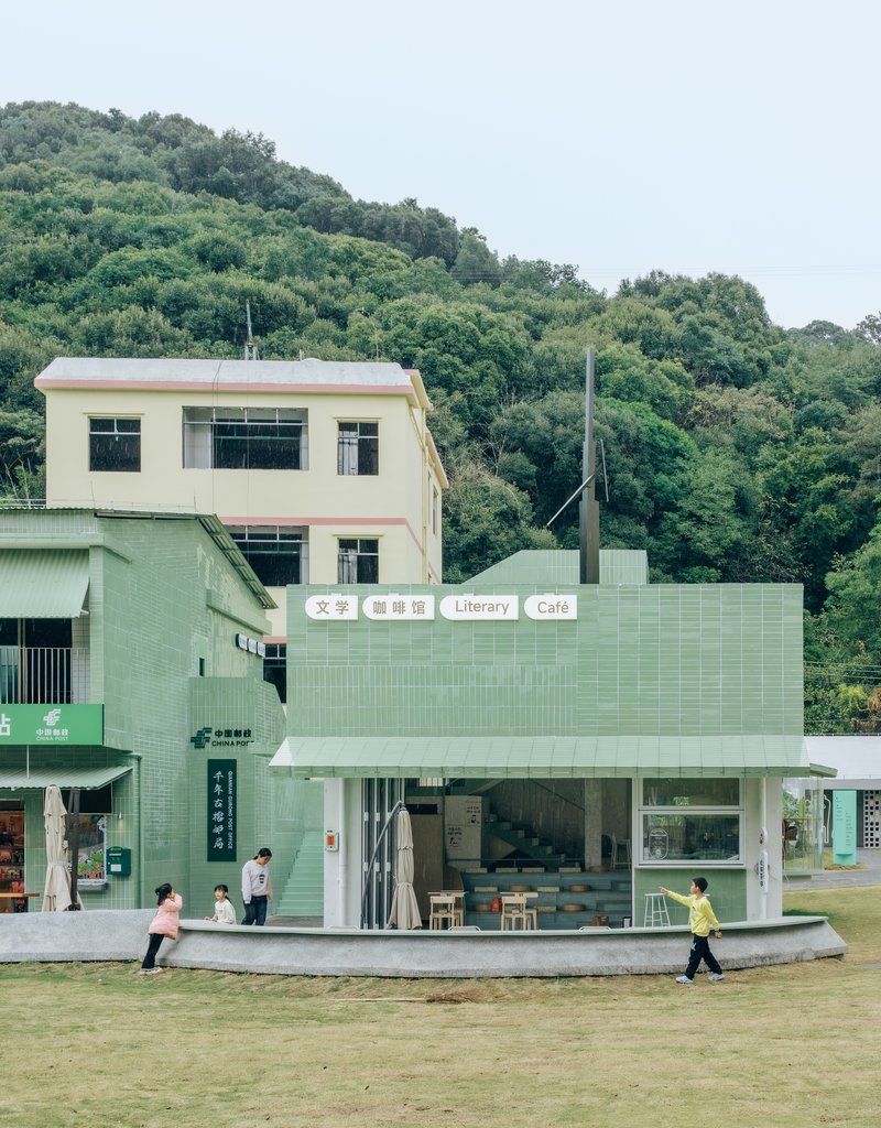 Single-storey library and cafe pavilion clad in pale green tiles with children running across the lawn