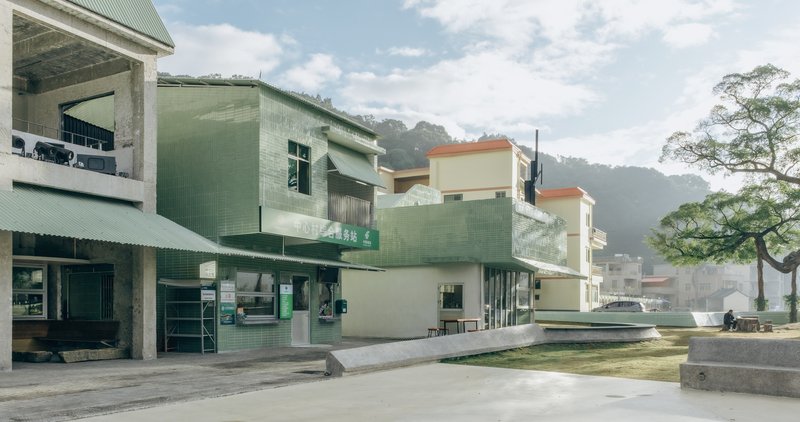 Public plaza with pale green corrugated metal buildings and concrete steps under partly cloudy skies