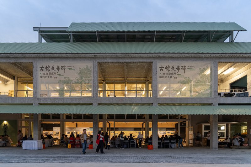 Two-storey facade with exposed timber beams, green corrugated roof and glazed infill panels at dusk