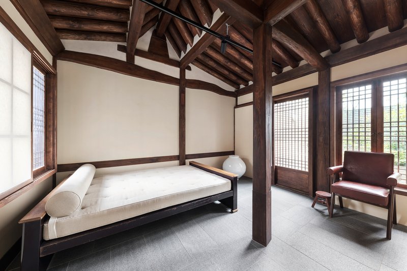 Bedroom with exposed timber post-and-beam structure, gridded sliding doors and white daybed beneath vaulted ceiling