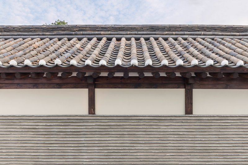 Detail of curved grey clay roof tiles above timber rafters and a white plaster wall