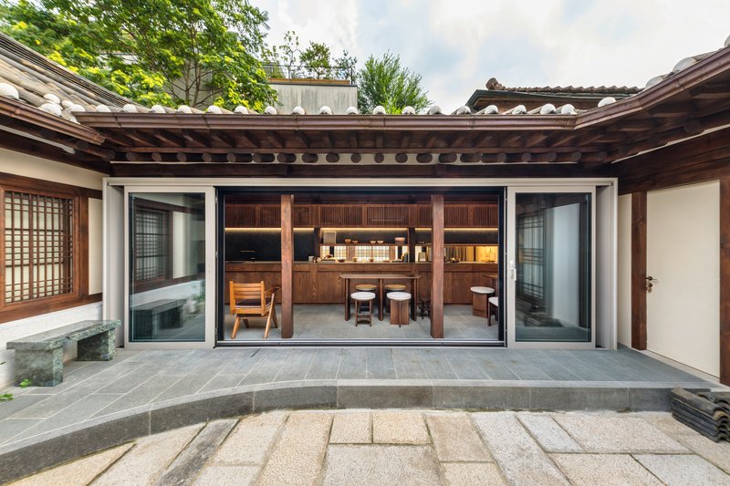 Courtyard view through open sliding glass doors into a timber kitchen with exposed rafter ceiling