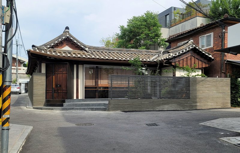Corner view showing the ribbed metal perimeter wall and curved tile roofline from the street