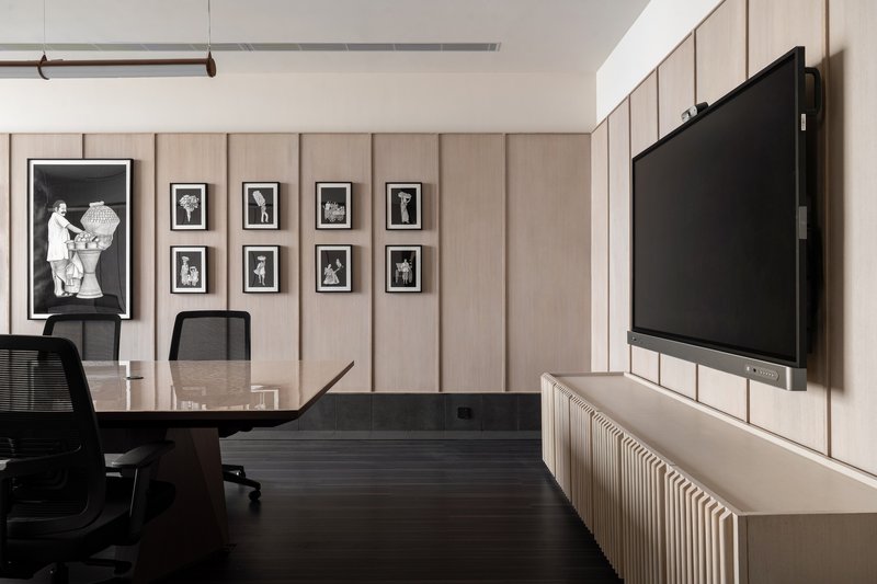 Conference room with vertical wood paneling displaying framed photographs and a wall-mounted screen