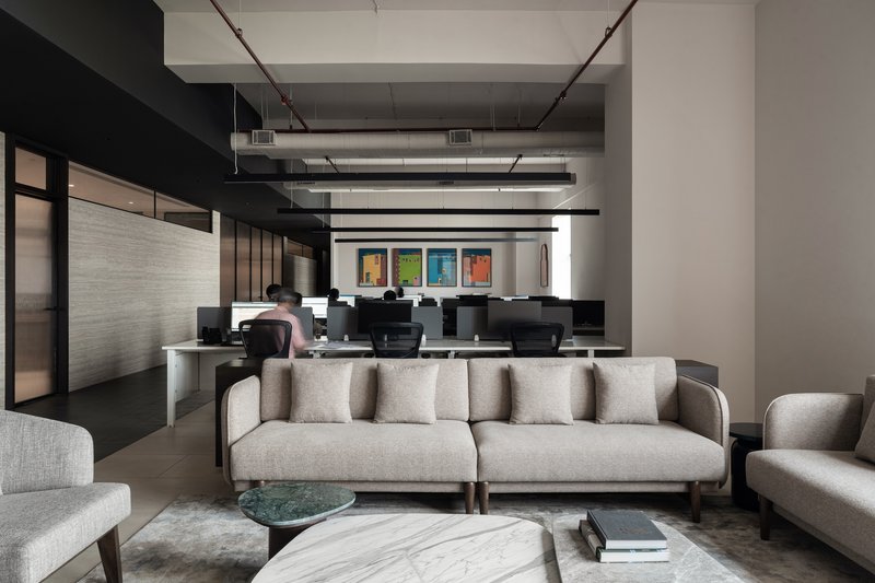 Lounge area with sofas and a marble coffee table overlooking workstations with exposed services