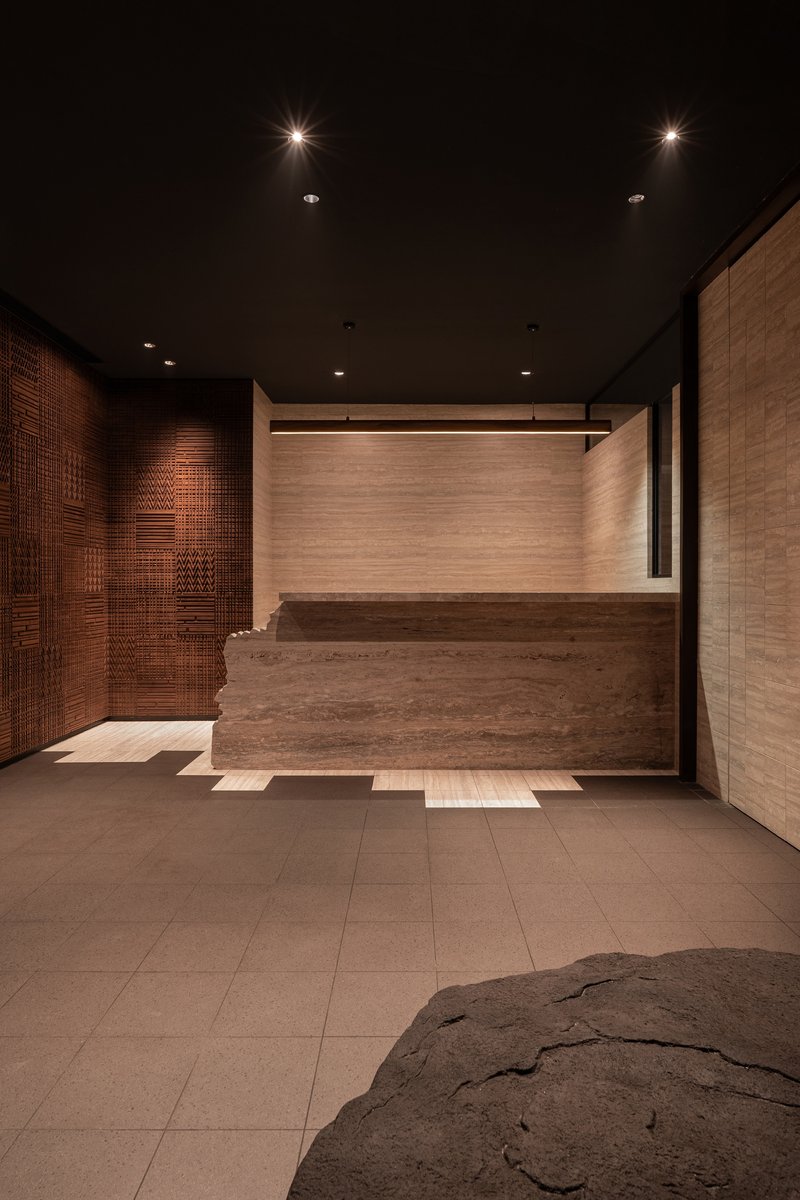 Reception desk in travertine stone with textured copper wall panels and recessed ceiling lighting