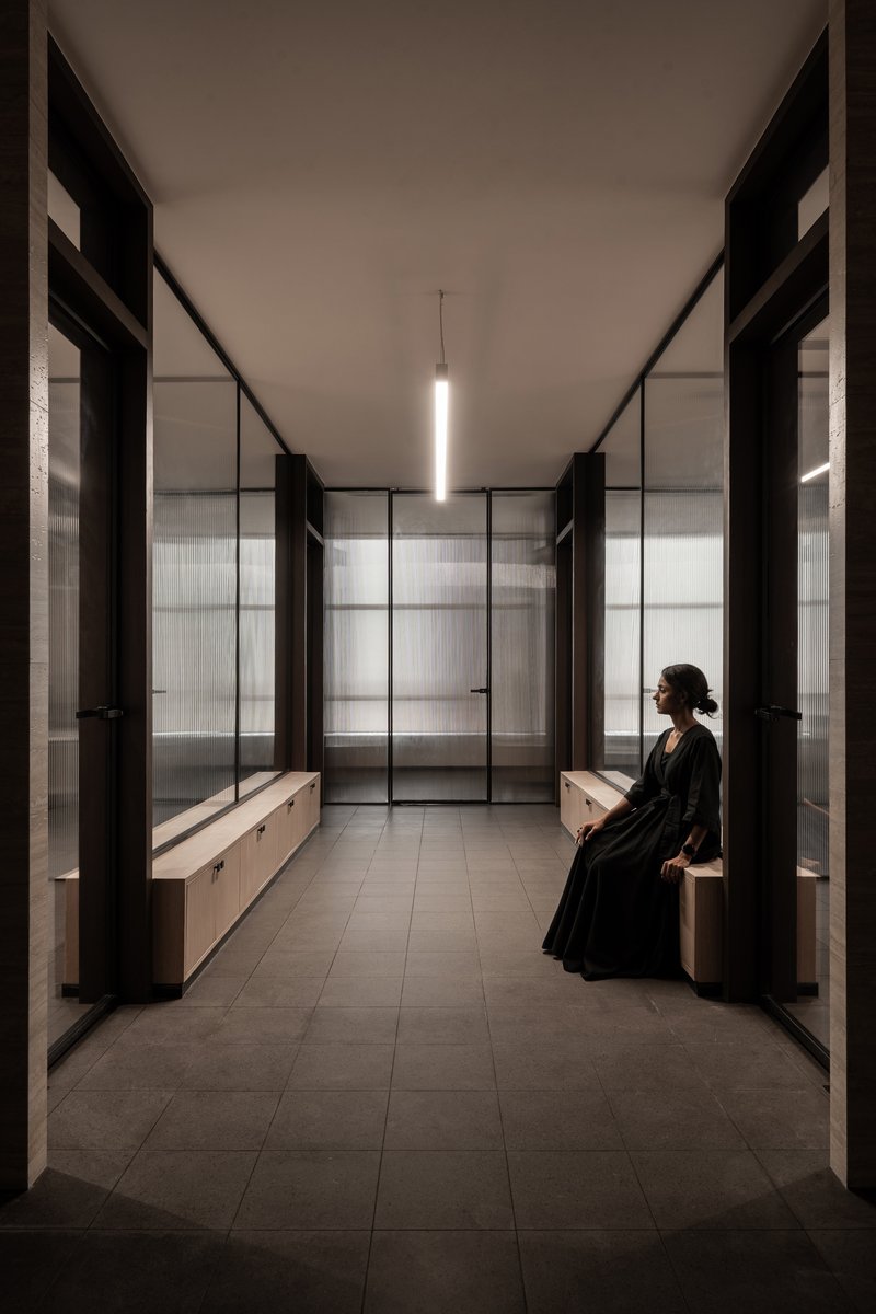Symmetrical fitting room with translucent glass partitions and a seated figure in black robes