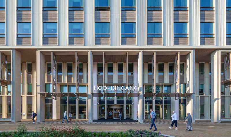 Ground-level entrance colonnade with vertical fins above and pedestrians crossing the plaza