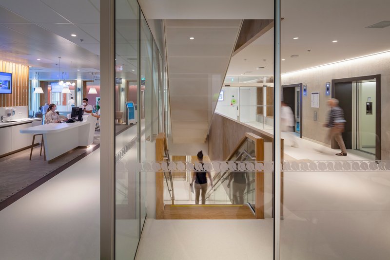 Timber staircase descending between glass partitions with people in motion near elevator banks