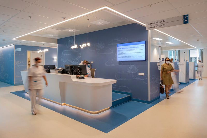 Reception desk under a house-shaped lighting canopy with staff and visitors passing through