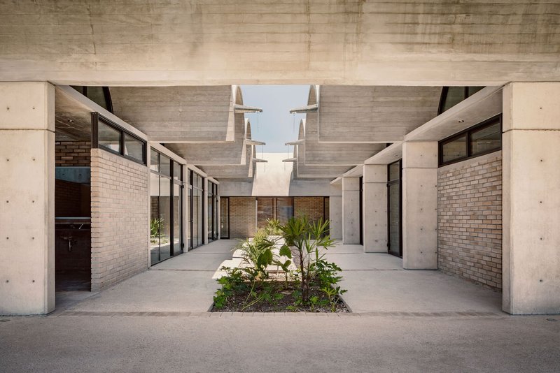 Interior courtyard with planted bed flanked by glazed corridors and paired sculptural skylights overhead