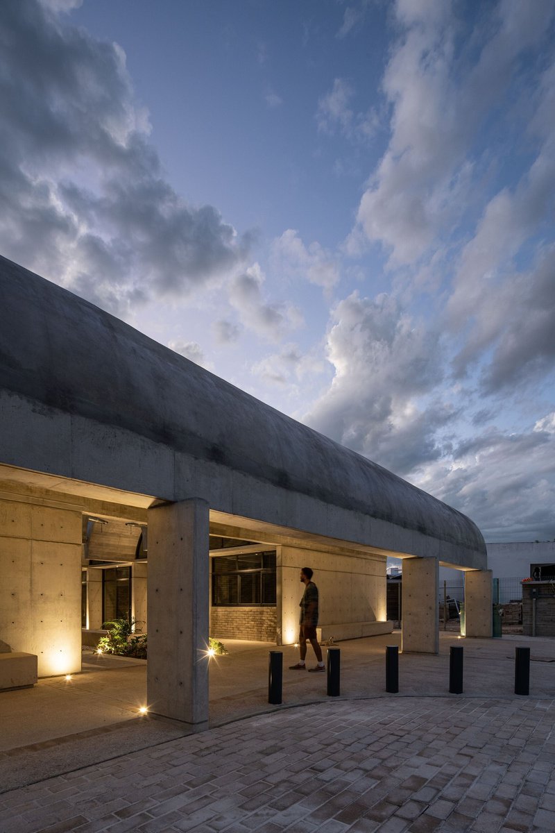 Covered porch with concrete vault and timber-lined soffit lit at dusk under dramatic clouds