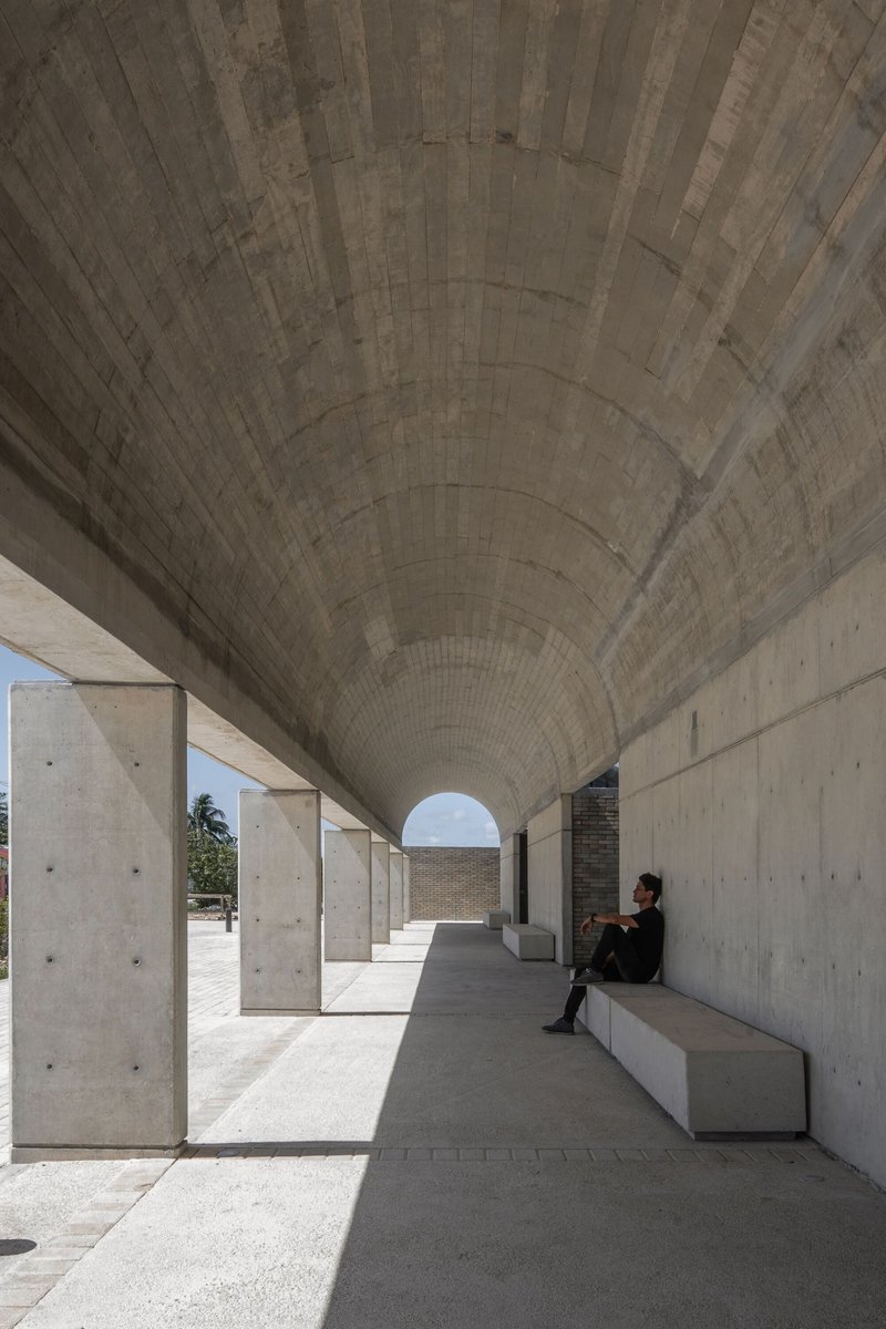 Barrel-vaulted concrete colonnade with person seated on bench in bright daylight