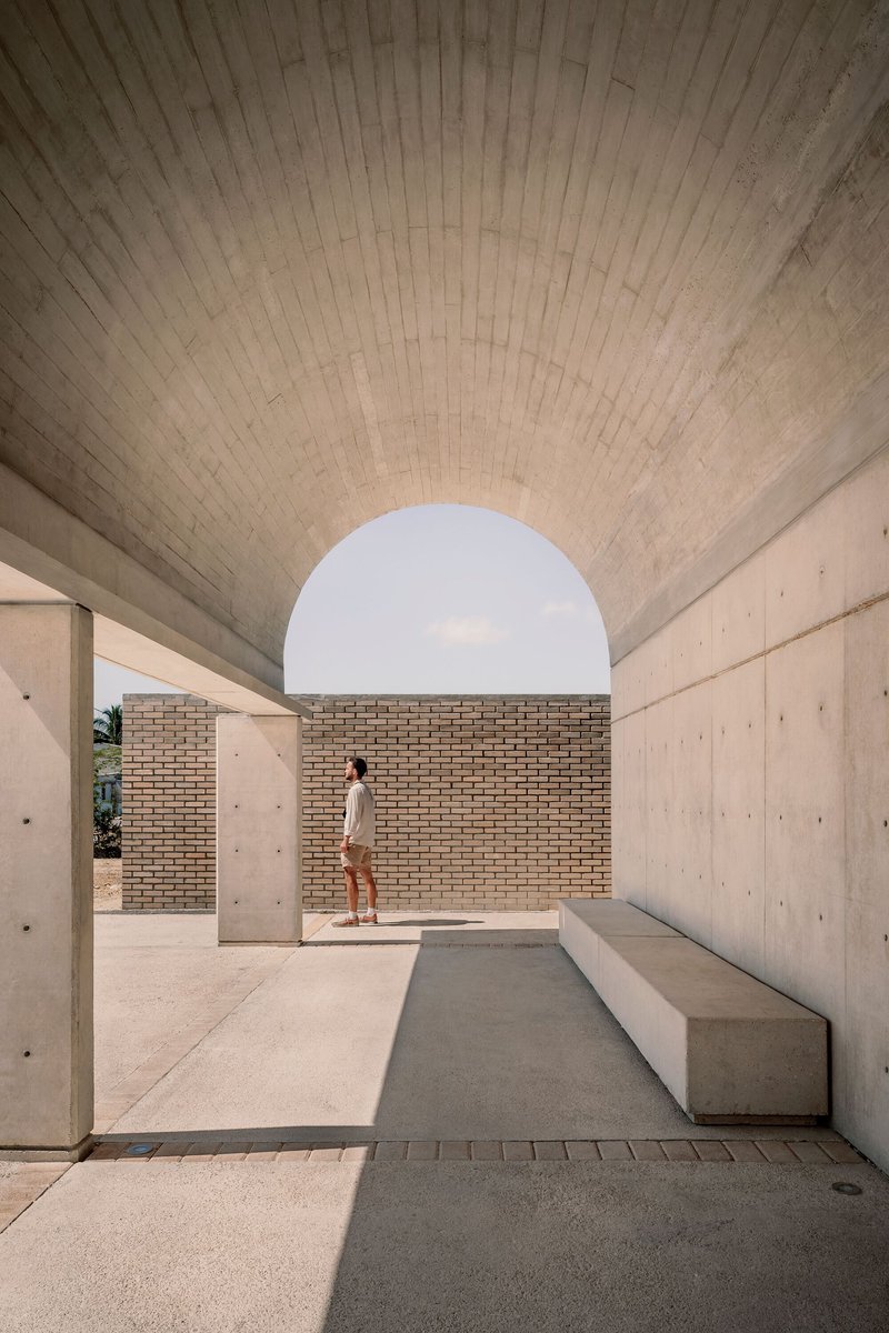 Covered passageway with board-formed concrete vault ceiling and circular opening framing a brick wall
