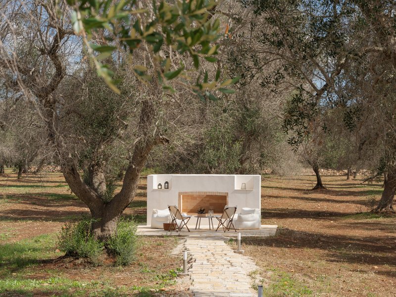 Freestanding white outdoor kitchen with arched opening in an olive grove under scattered clouds