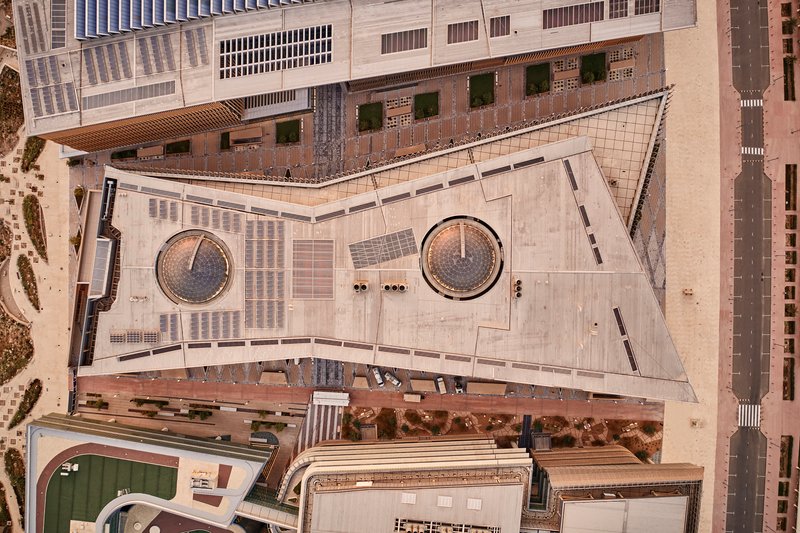 Aerial view of triangular concrete plaza with two circular planters and pedestrians below