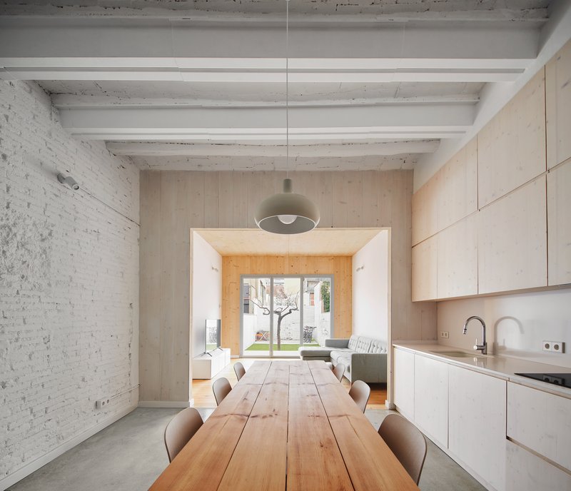 Dining area with timber table beneath exposed white ceiling beams and painted brick wall