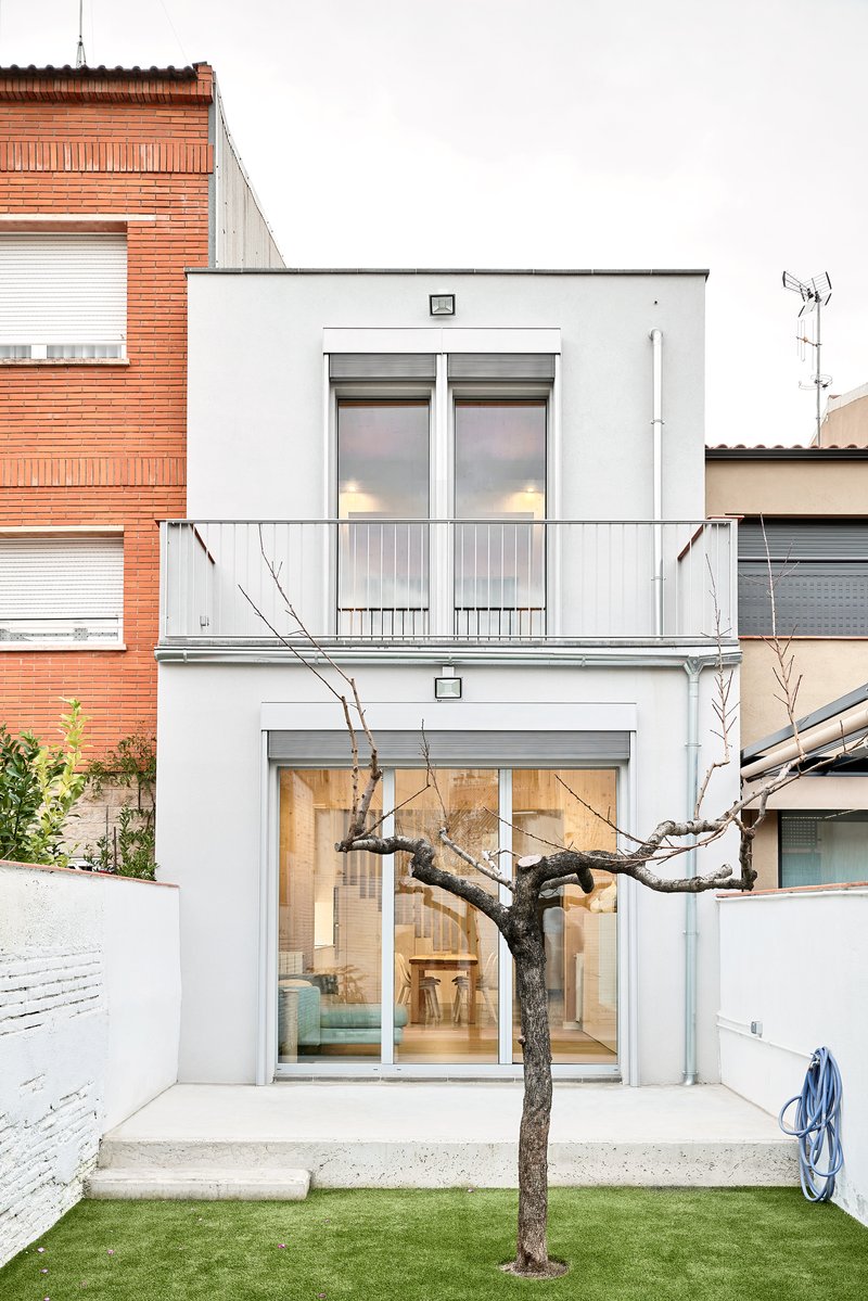 Rear facade with white stucco walls and glazed doors opening to courtyard with bare tree