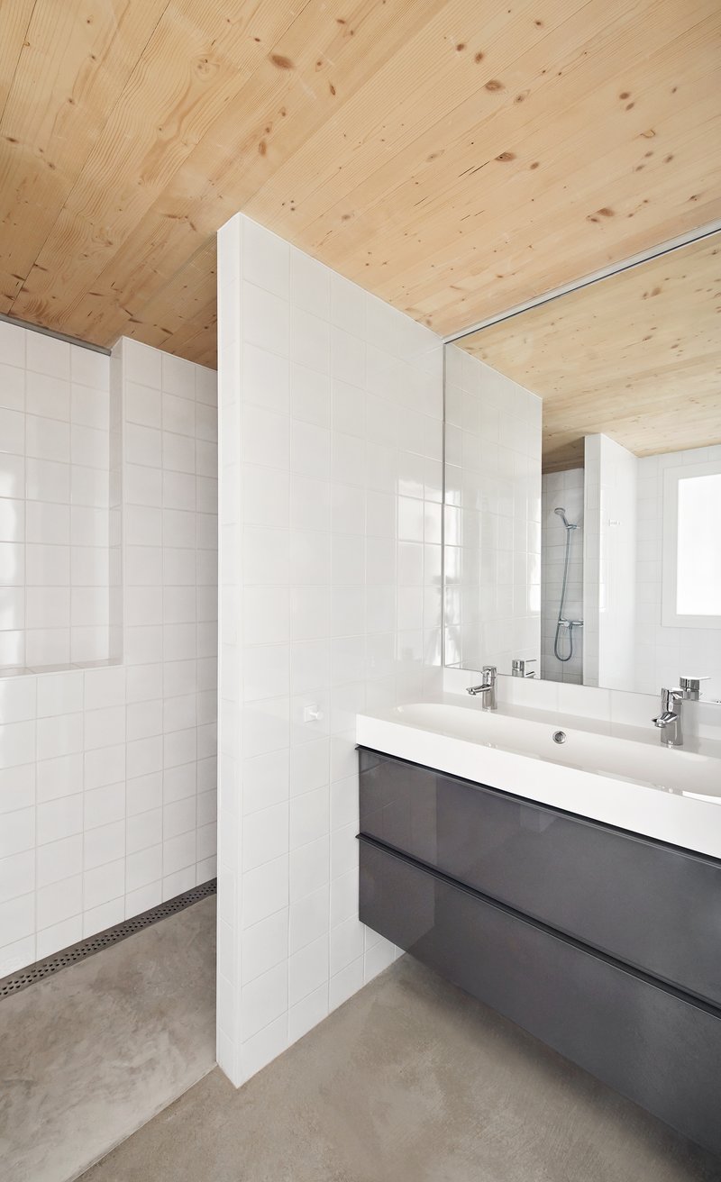 Bathroom with white tile walls, double vanity and plywood ceiling above polished concrete floor