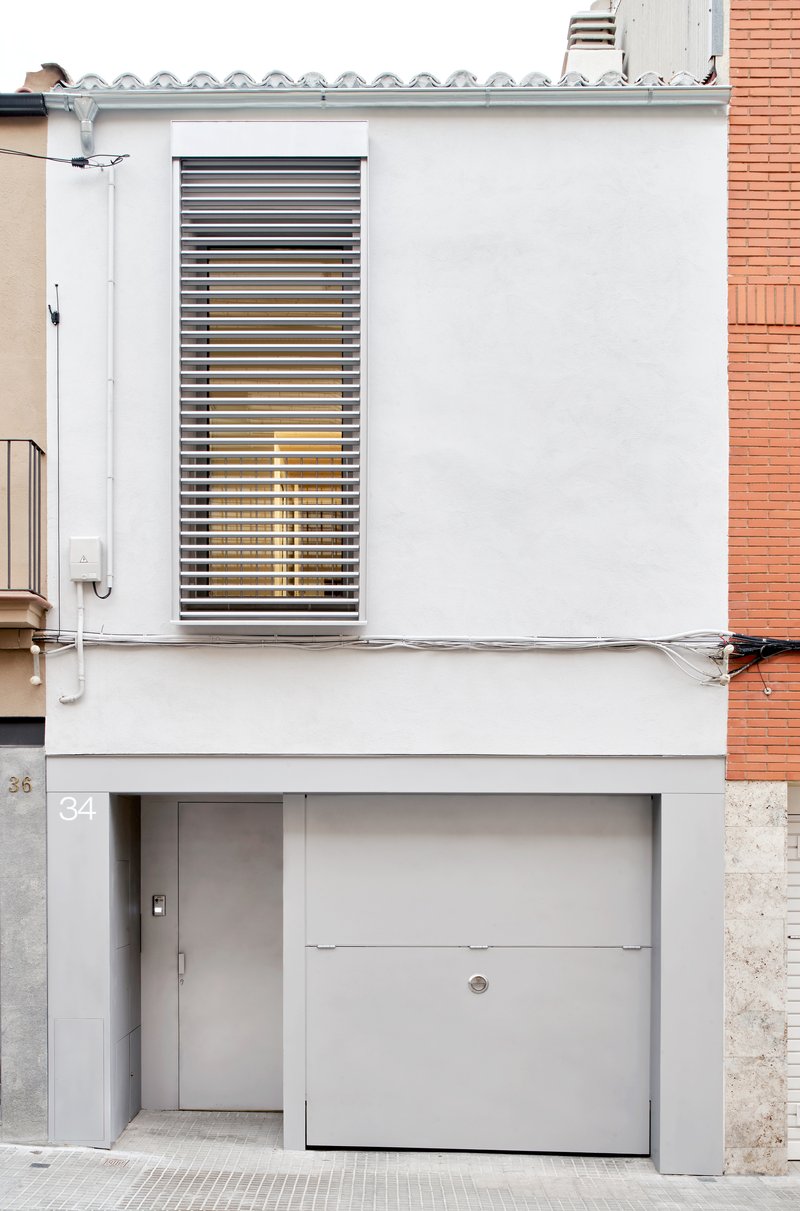 Street facade with white stucco, louvered window, garage door and neighbouring terracotta brickwork