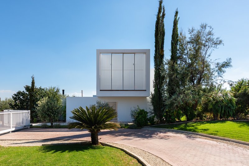 White two-story volume with vertical louver screen surrounded by cypress trees and curved paved driveway