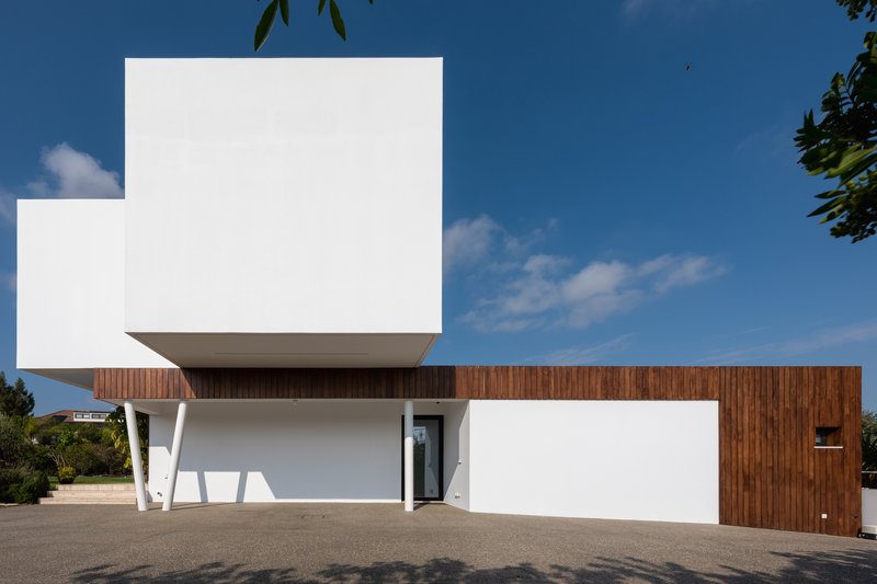 Street facade with cantilevered white volume above recessed entry and vertical timber cladding under clear sky