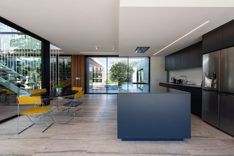 Open-plan kitchen and dining area with dark island, yellow chairs, and floor-to-ceiling glass overlooking a courtyard