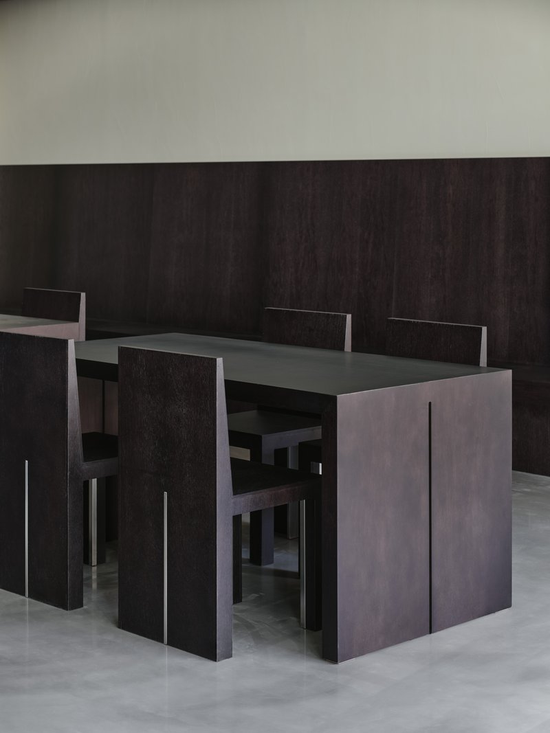 Close-up of black wood table and chairs against a dark paneled wall in even light