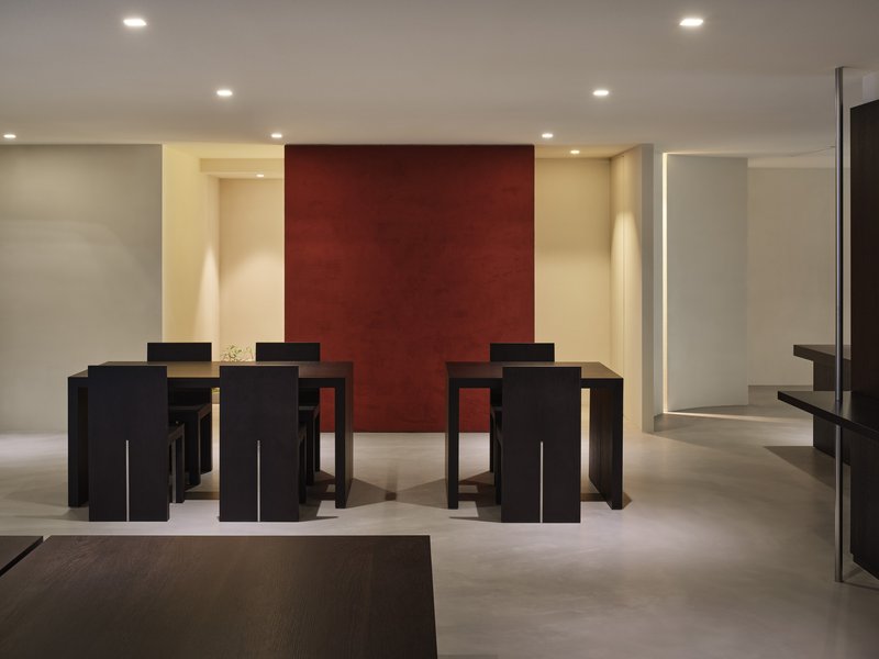 Multiple black dining tables arranged before a deep red accent wall in a pale interior