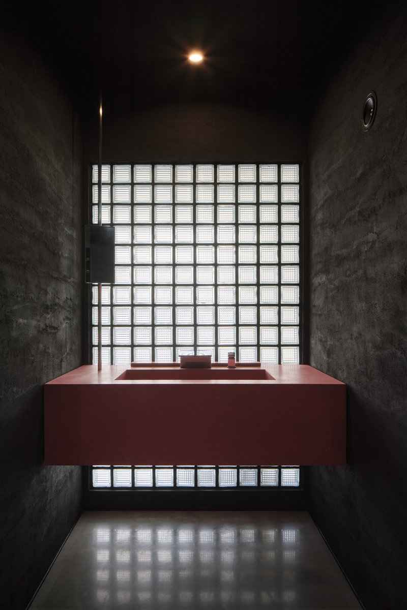 Maroon rectangular basin beneath a glass block window in a dark concrete chamber with reflected light below