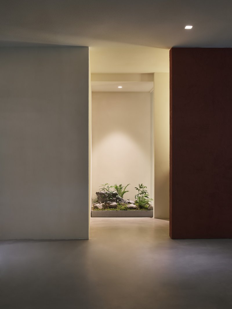 Interior corridor framing a backlit planter niche with small potted plants and grey tiled floor