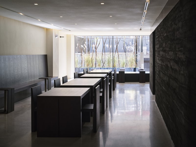 Dining room with dark tables facing a courtyard window lined with bare trees