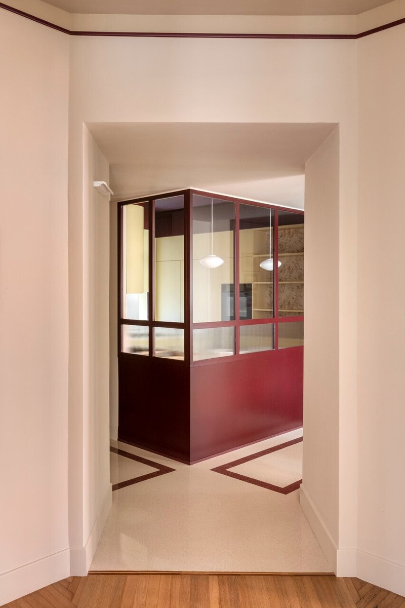 Framed view of a maroon and glass partition wall with pendant lights visible through the glazing