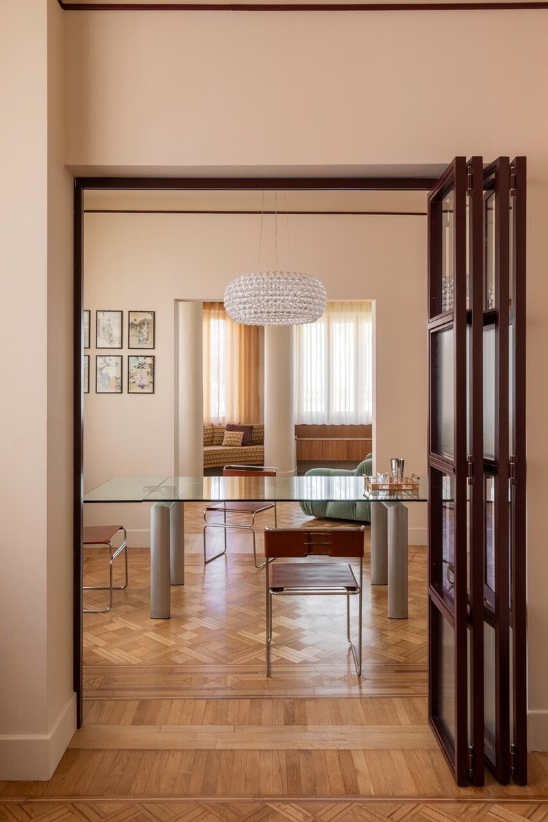 Dark wood folding screen doors opening to reveal a glass dining table with cylindrical metal legs