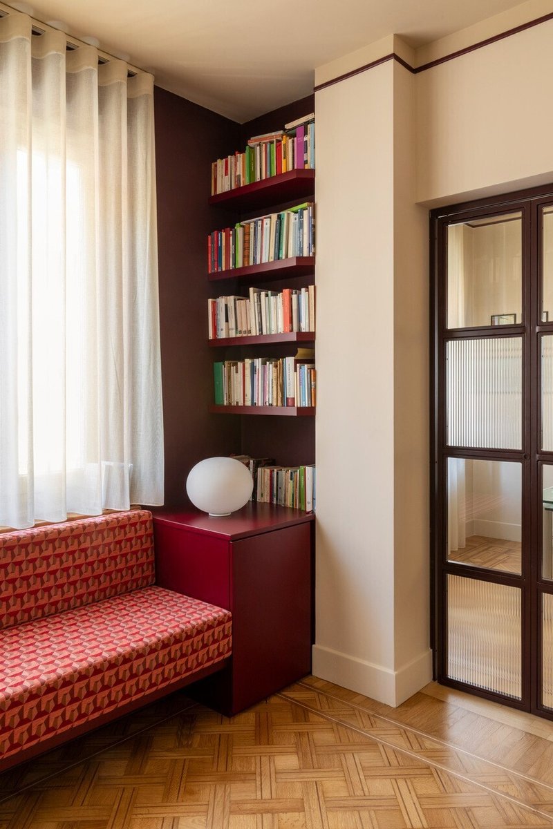 Corner reading nook with maroon built-in shelves filled with books beside a glazed door panel