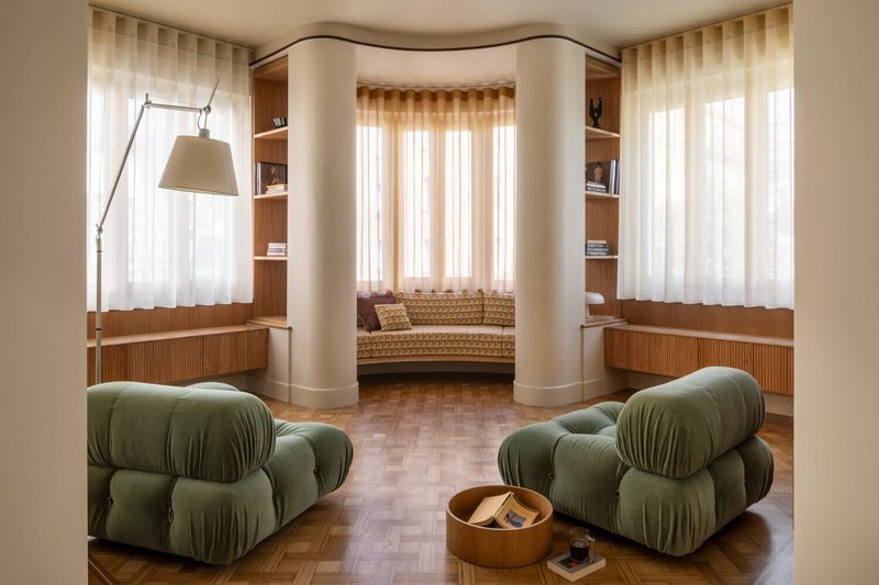 Paired white columns flanking a curved window alcove with built-in timber cabinetry beneath sheer drapes