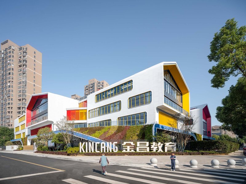 Street view of the white facade with curved forms and colored panels against highrise residential towers