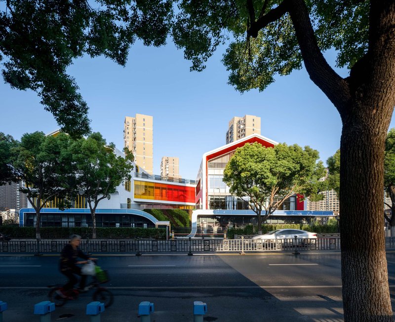 Street view framed by mature trees with a cyclist passing in front of the raised complex