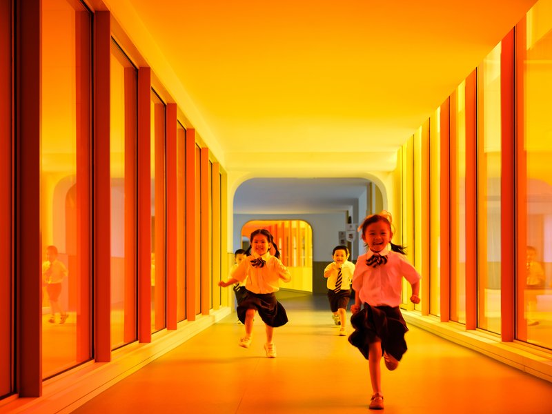 Orange-lit corridor with vertical mullions and children running through the space