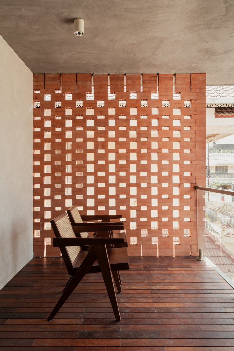 Timber lounge chair on deck facing perforated brick wall with exposed concrete soffit overhead