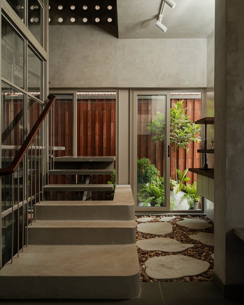 Interior stair with circular stepping stones in gravel courtyard and potted plants beside glass doors