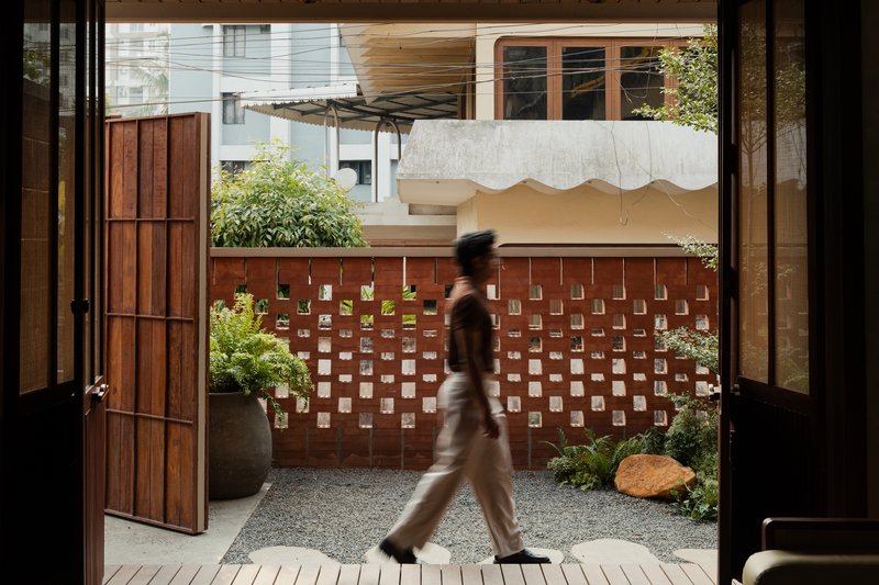View through open doors to gravel courtyard with perforated brick wall and figure walking past