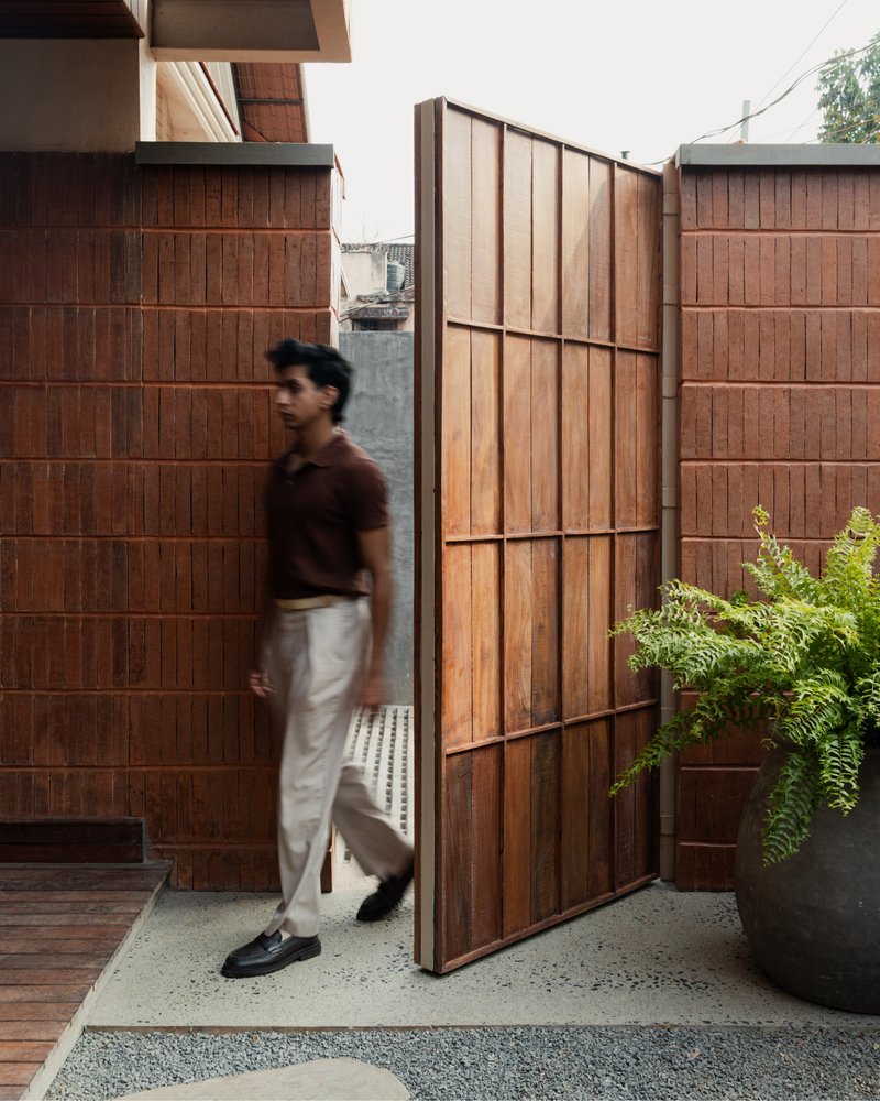 Pivoting timber screen with black metal frame beside tiled walls and a figure in motion