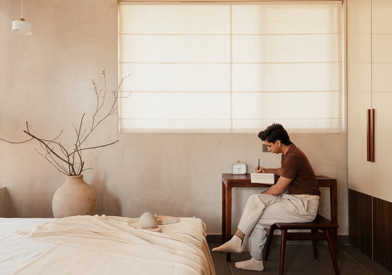 Bedroom workspace with person at writing desk beneath a translucent fabric roman shade