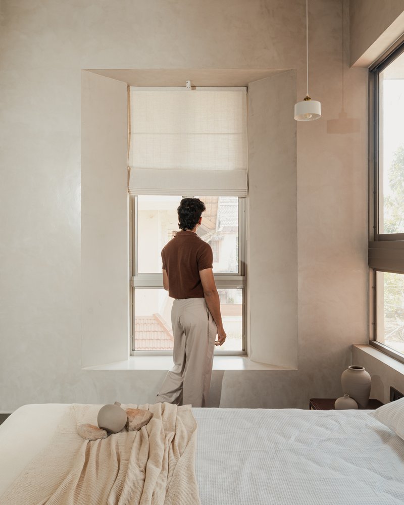 Tall recessed window niche with person looking out over bed and cream-toned plastered walls