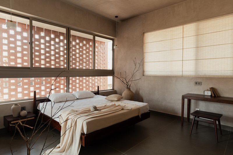 Bedroom with perforated terracotta brick window wall filtering soft daylight onto polished concrete floors