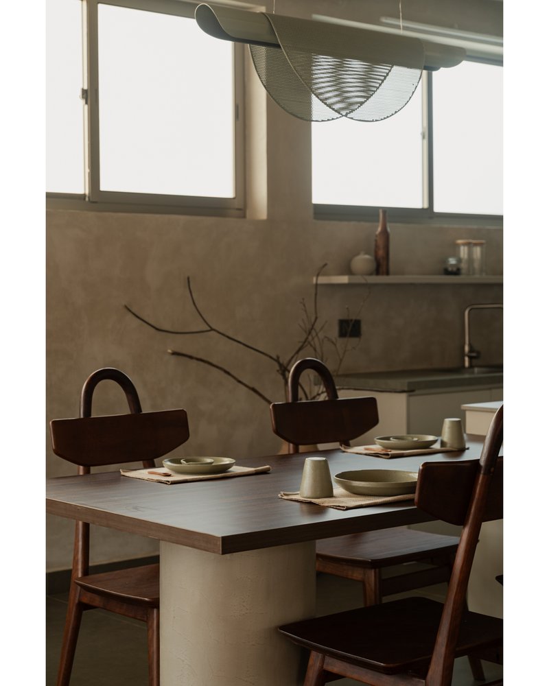 Close-up of dining table set with ceramic vessels and curved timber basket handles beneath wire pendant light