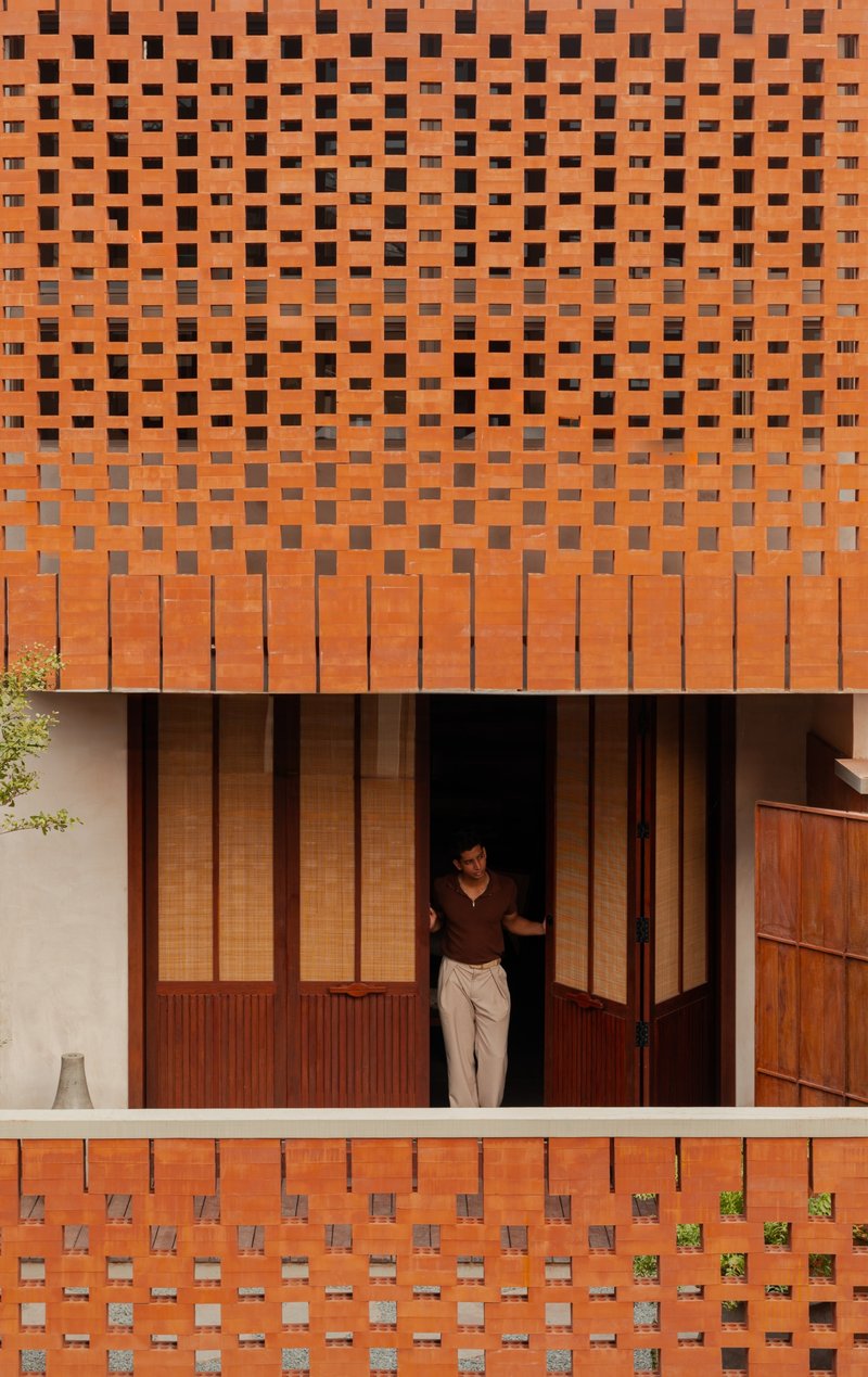Perforated terracotta brick facade with a person standing in the recessed timber doorway