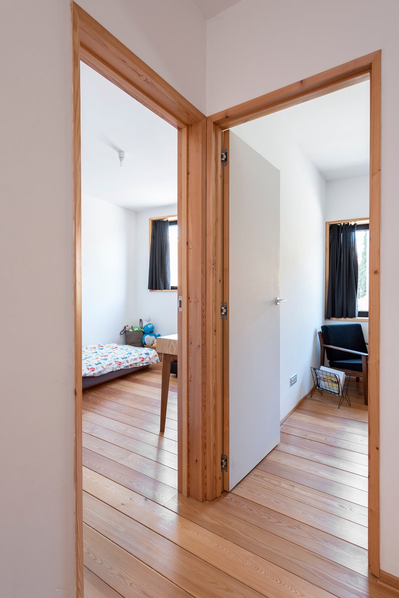 View through timber-framed doorways connecting bedroom and living spaces with white walls and timber floors